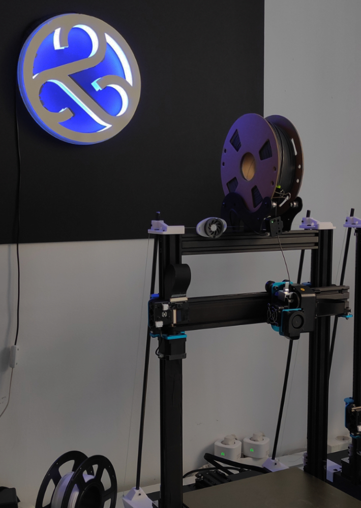 imagen del taller con el logo de to infinity iluminado y una impresora 3d iluminada por la luz azul del logo